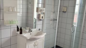 A modern bathroom with a glass-enclosed shower, white tiled walls, a white sink, and a mirror.