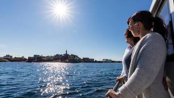 A boat with two passengers looking at a coastal town with buildings and a lighthouse.