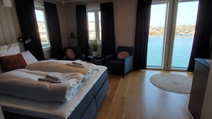 A hotel room with a large bed, a desk, a chair, and a view of the sea.