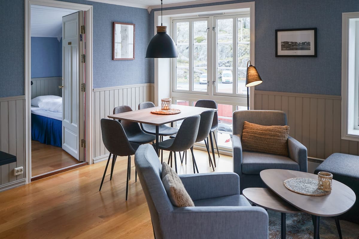 A room with a dining table, chairs, a sofa, and a small table with a lamp.