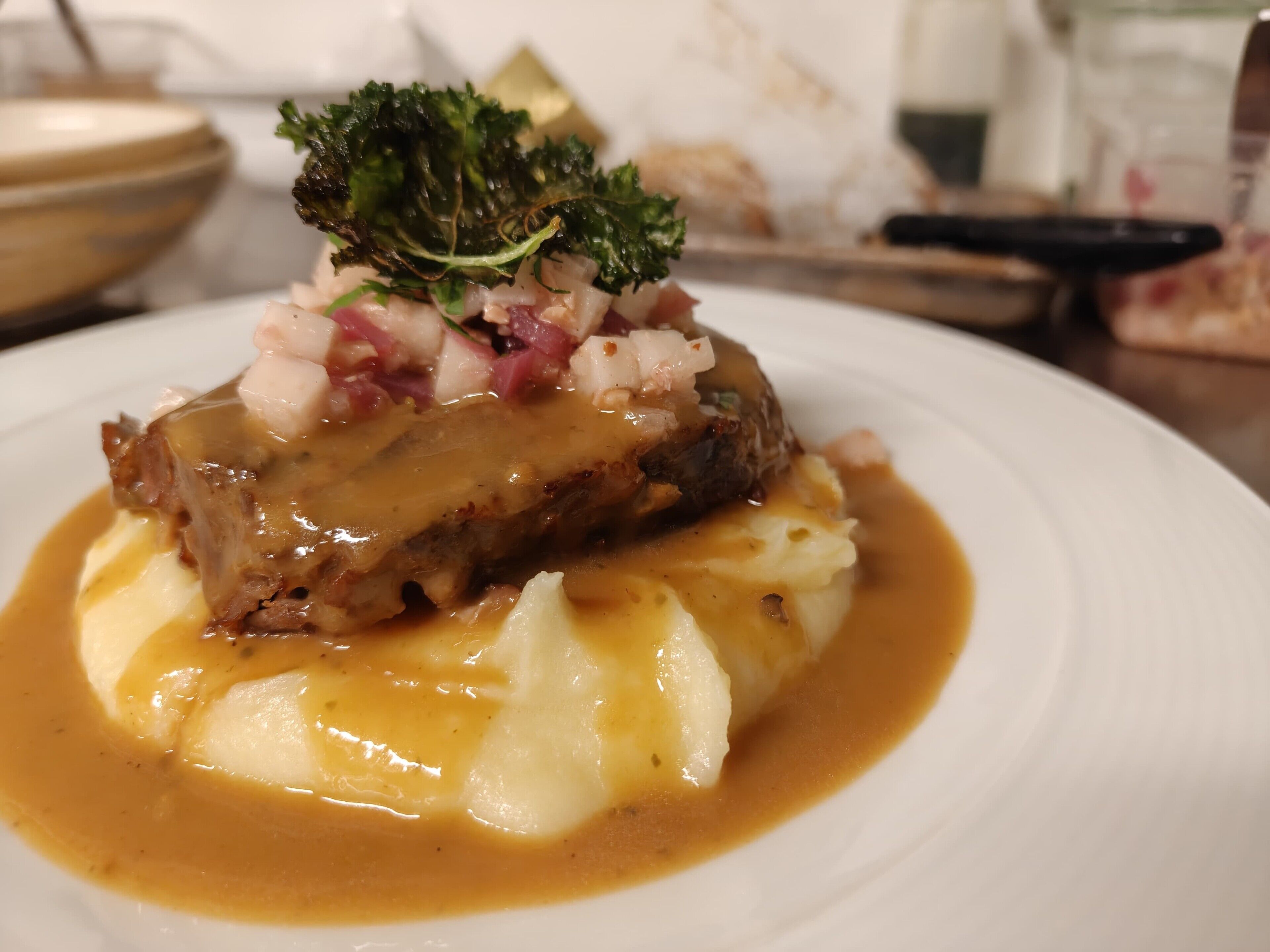 A plate of food with a meat dish, mashed potatoes, and a garnish.