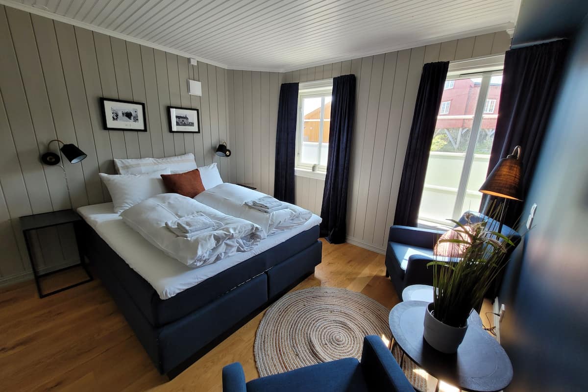 A modern bedroom with a large bed, a small seating area, and a view of the outside.