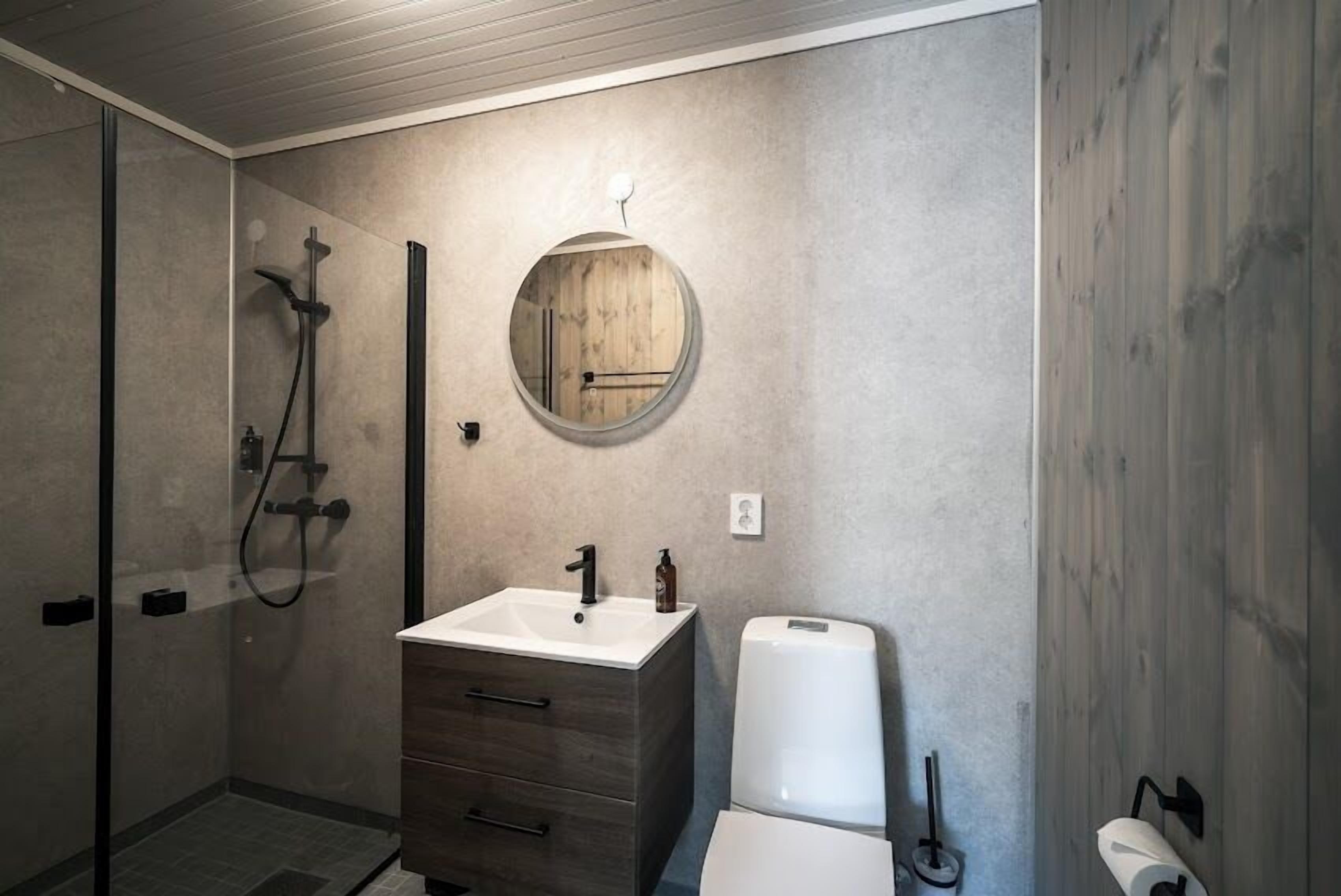 Un bagno moderno con cabina doccia in vetro, mobile bagno in legno con lavandino e un water.