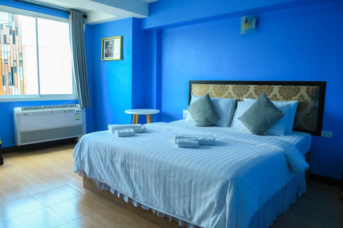 A hotel room with a large bed, a small round table, a window with curtains, and a radiator.