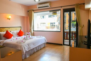 A hotel room with a bed, a desk, a window with curtains, and an air conditioning unit.