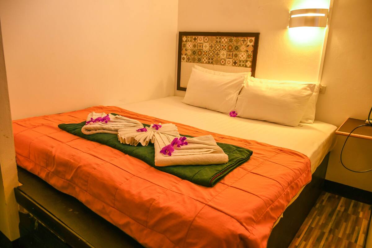 A hotel room with a neatly made bed, a green throw blanket, and towels arranged on the bed.