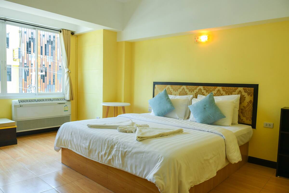 A hotel room with a bed, a window with curtains, a small table, and a heater.