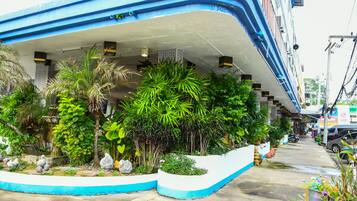 A hotel with a blue and white facade, lush greenery, and a concrete pathway.