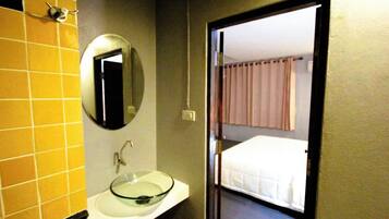 Un baño con un lavabo de vidrio, un espejo y una puerta que da a un dormitorio con cama y cortinas.