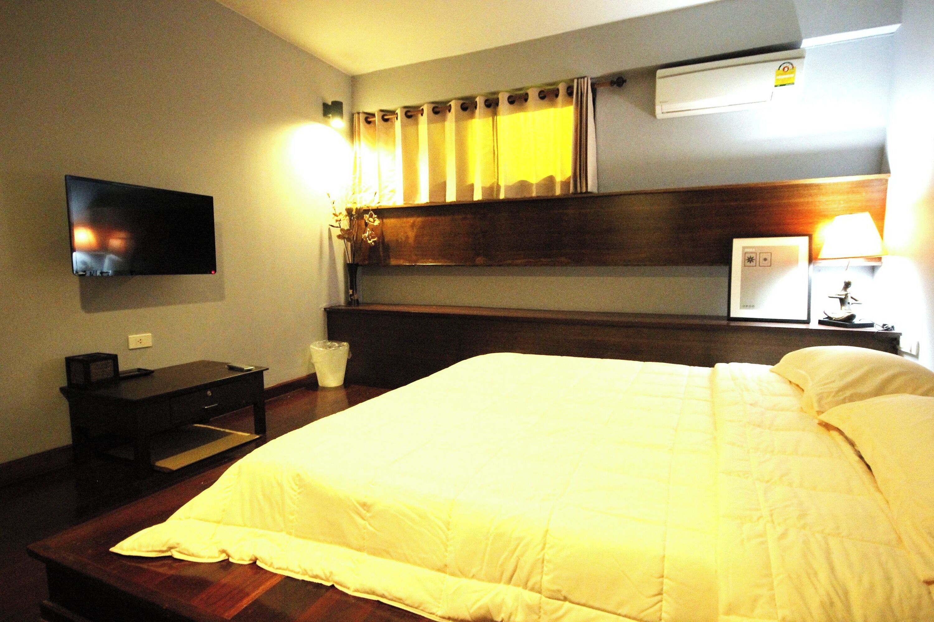 Habitación de hotel con una cama grande, un televisor de pantalla plana montado en la pared, una mesita de noche, una lámpara y un equipo de aire acondicionado.