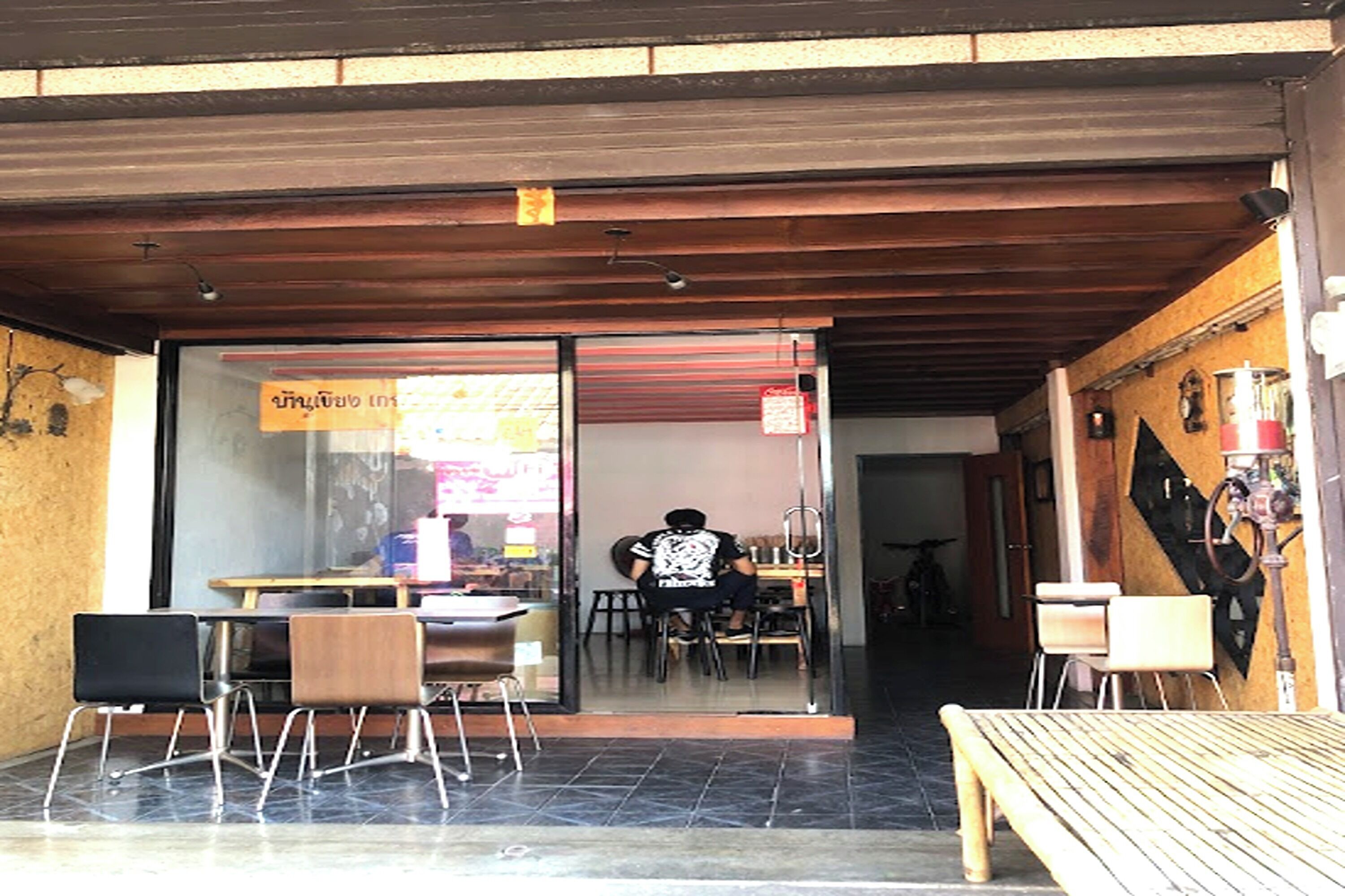 An outdoor seating area with tables and chairs, a person sitting inside, and a bicycle in the background.