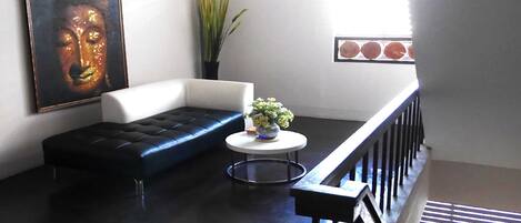 Una sala moderna con un sofá de cuero negro, un sillón blanco, una mesa de centro redonda con un florero y un cuadro grande de Buda en la pared.