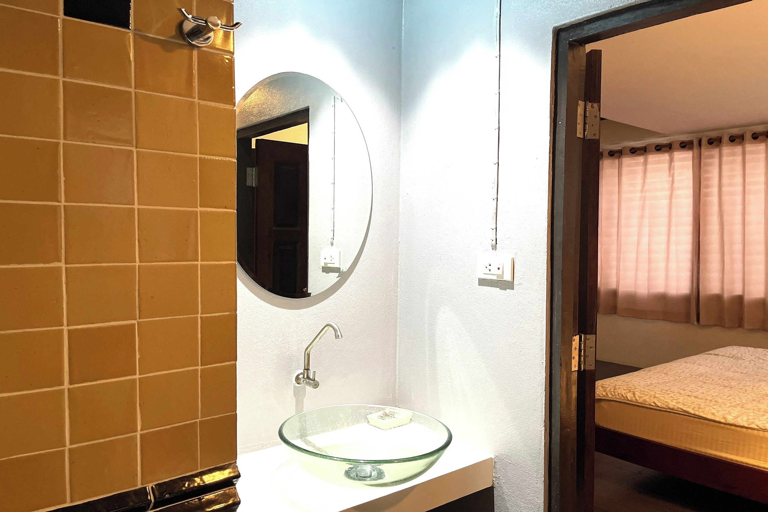 A bathroom with a glass sink, a mirror, and a bed visible through an open door.