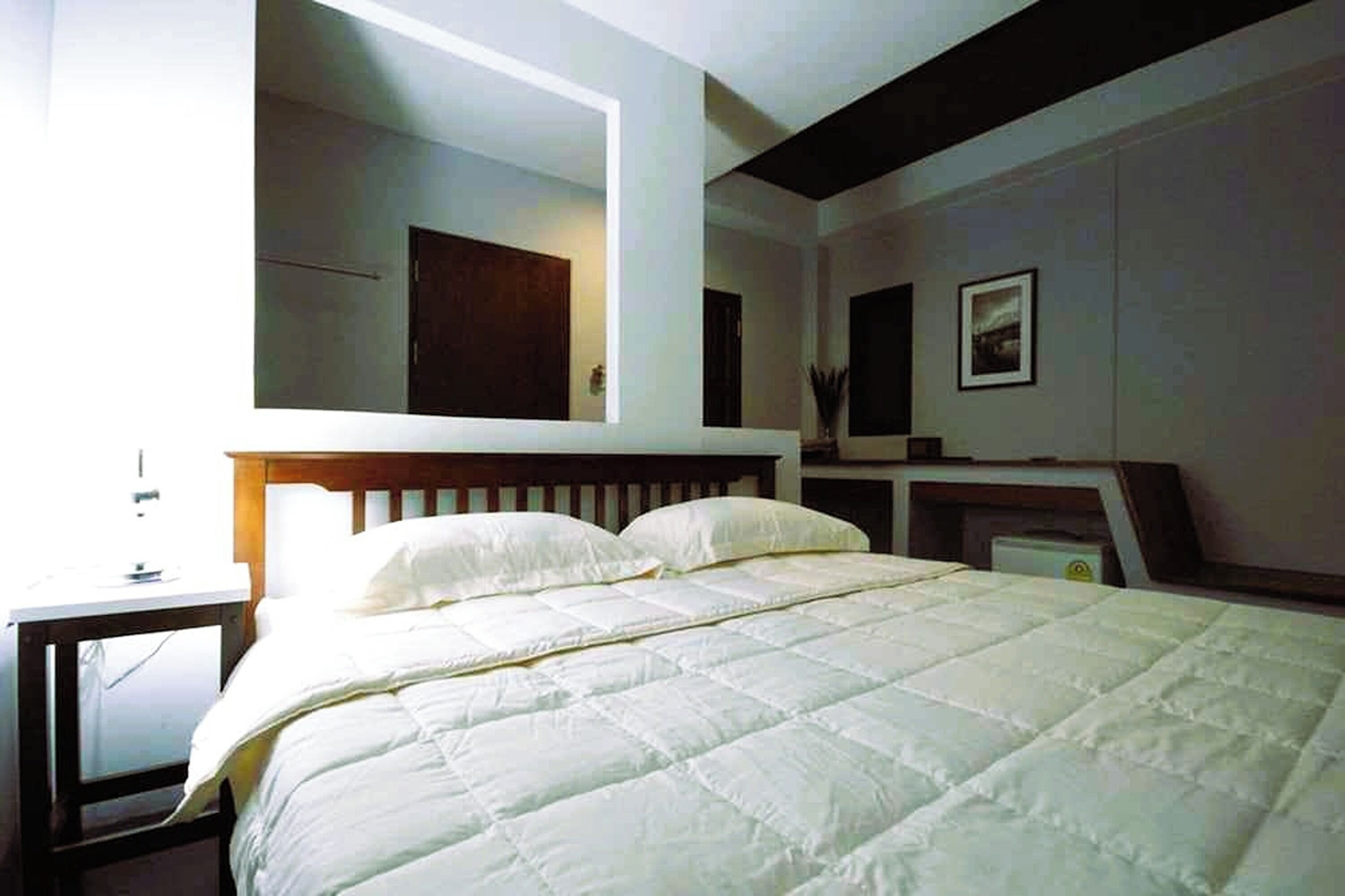 A bedroom with a large bed, a bedside table, a mirror, and a framed picture on the wall.