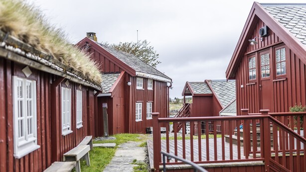 A row of red wooden buildings with a stone pathway and wooden benches. - Håholmen Havstuer - by Classic Norway Hotels (Averoy)