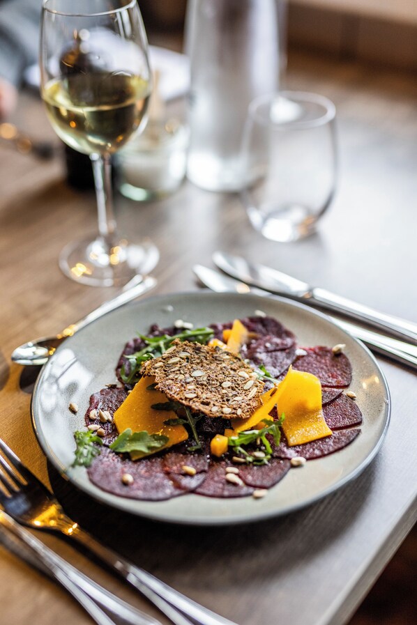 A plate of food with a variety of vegetables and grains, accompanied by a glass of white wine. - Håholmen Havstuer - by Classic Norway Hotels (Averoy)