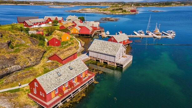 A coastal village with traditional red houses, a dock with boats, and clear blue waters. - Håholmen Havstuer - by Classic Norway Hotels (Averoy)