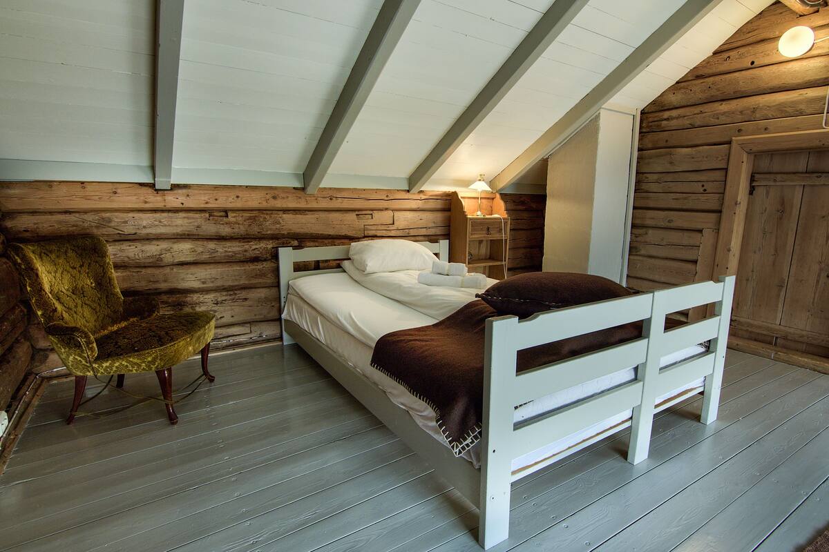 Un dormitorio tipo cabaña de madera con una cama individual, una silla y una mesita de noche con una lámpara.