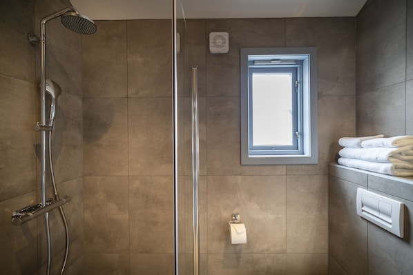 A bathroom with a shower, a towel rack, and a toilet paper holder. - Håholmen Havstuer - by Classic Norway Hotels (Averoy)