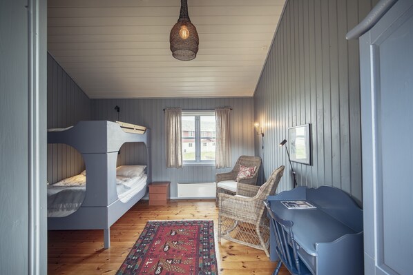 A compact bedroom with bunk beds, a blue sofa, a wicker chair, and a patterned rug. - Håholmen Havstuer - by Classic Norway Hotels (Averoy)