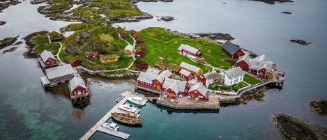 An aerial view of a coastal village with traditional red-roofed buildings, a dock with boats, and clear blue waters.
