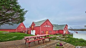 A red wooden building with a picnic table and potted plants on a wooden deck by a body of water. - Håholmen Havstuer - by Classic Norway Hotels (Averoy)