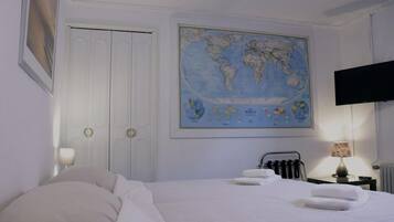 Een net opgemaakt bed met witte lakens, een wereldkaart aan de muur, een flatscreen-tv en een radiator.