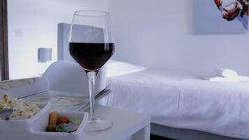 A glass of red wine on a white table with a bed and a painting in the background.