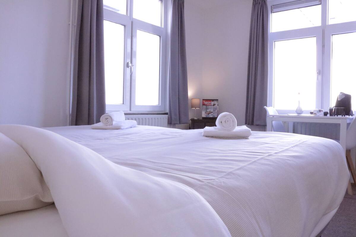 A hotel room with two beds, a desk, and a window with curtains.