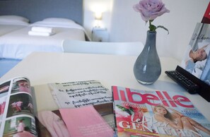 A hotel room with a bed, a vase with a flower, a magazine, and a remote control on the table.