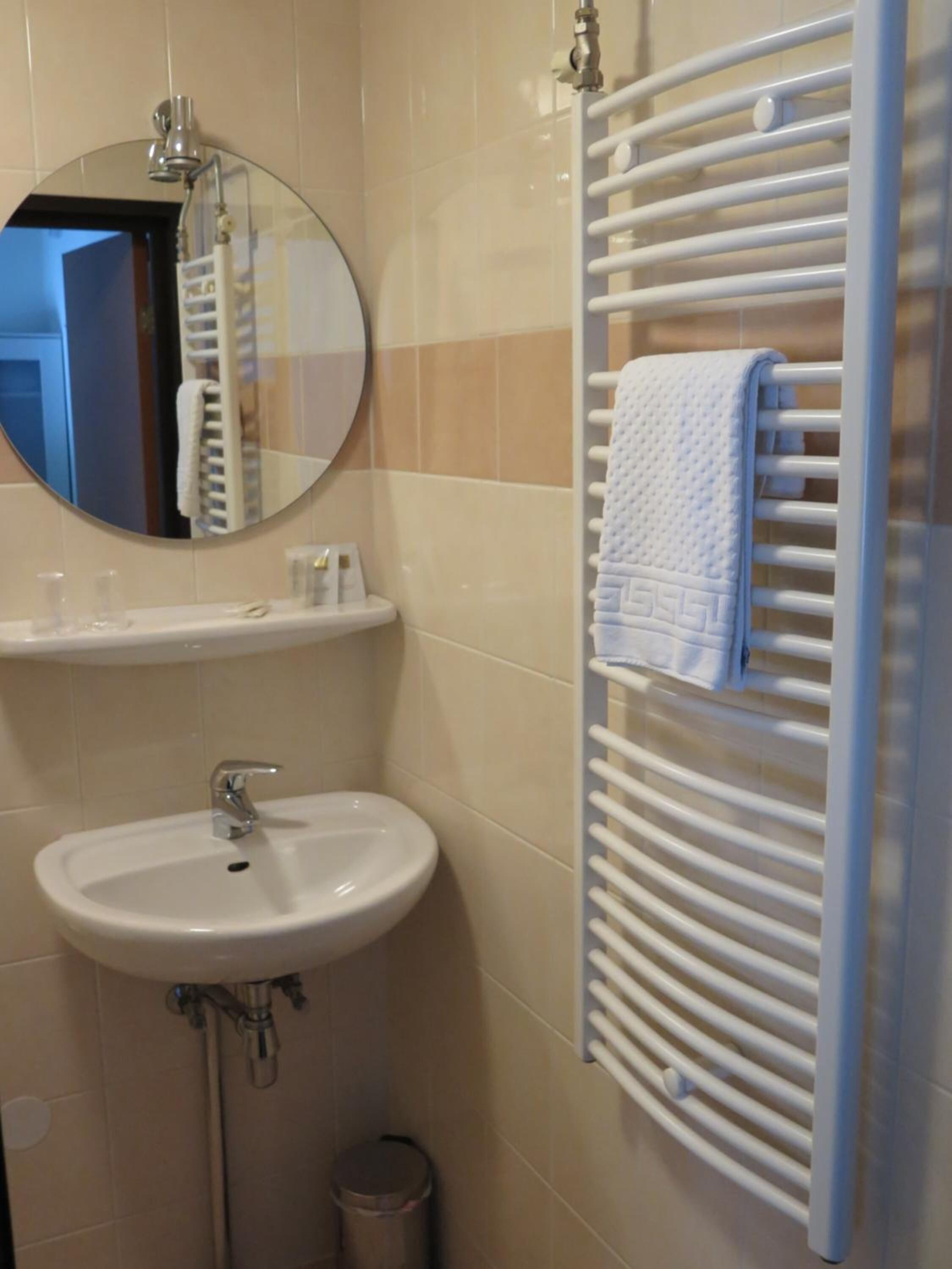 Een badkamer met een ronde spiegel, een wastafel, een handdoekhouder en een toilet.