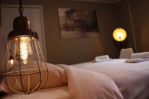 A hotel room with a bed, a hanging light fixture, a wall-mounted lamp, and a framed picture on the wall.