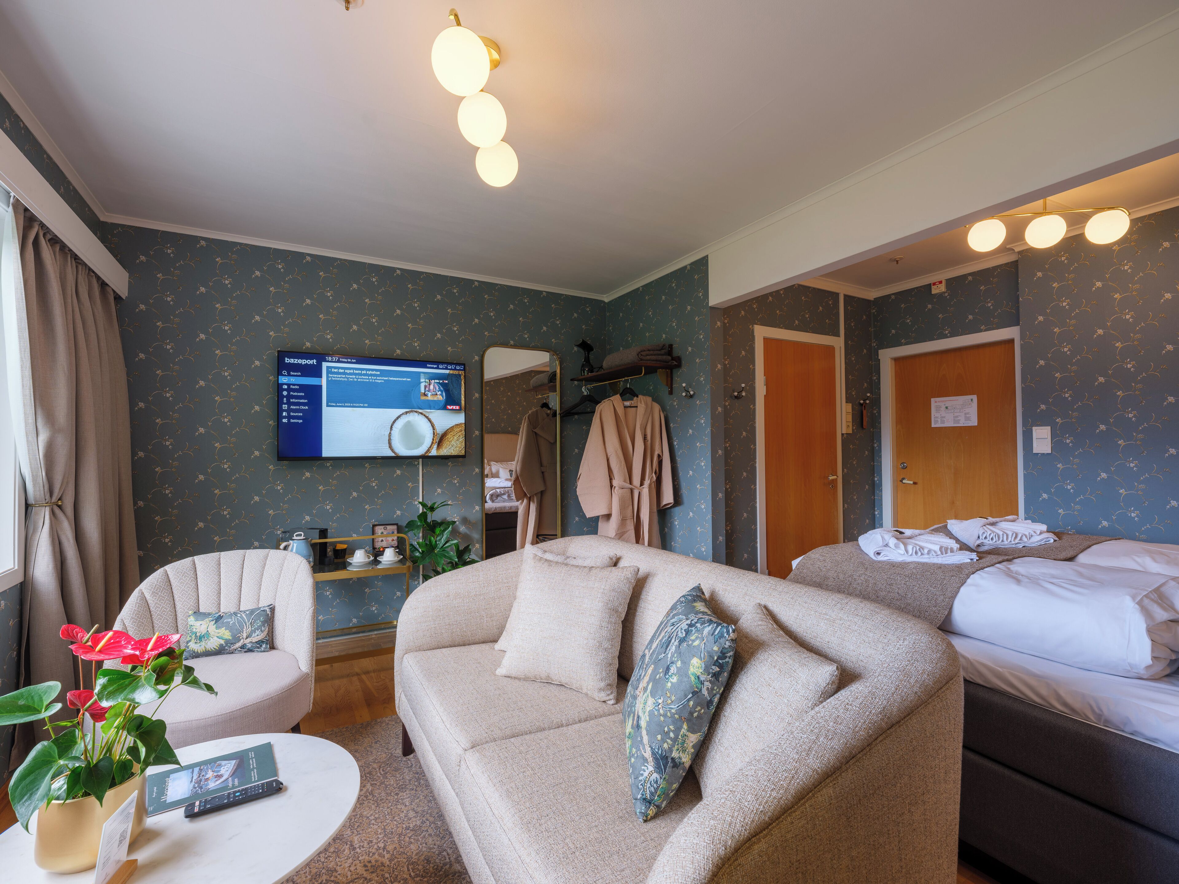 A hotel room with a sofa, a bed, a TV, a mirror, and a plant.