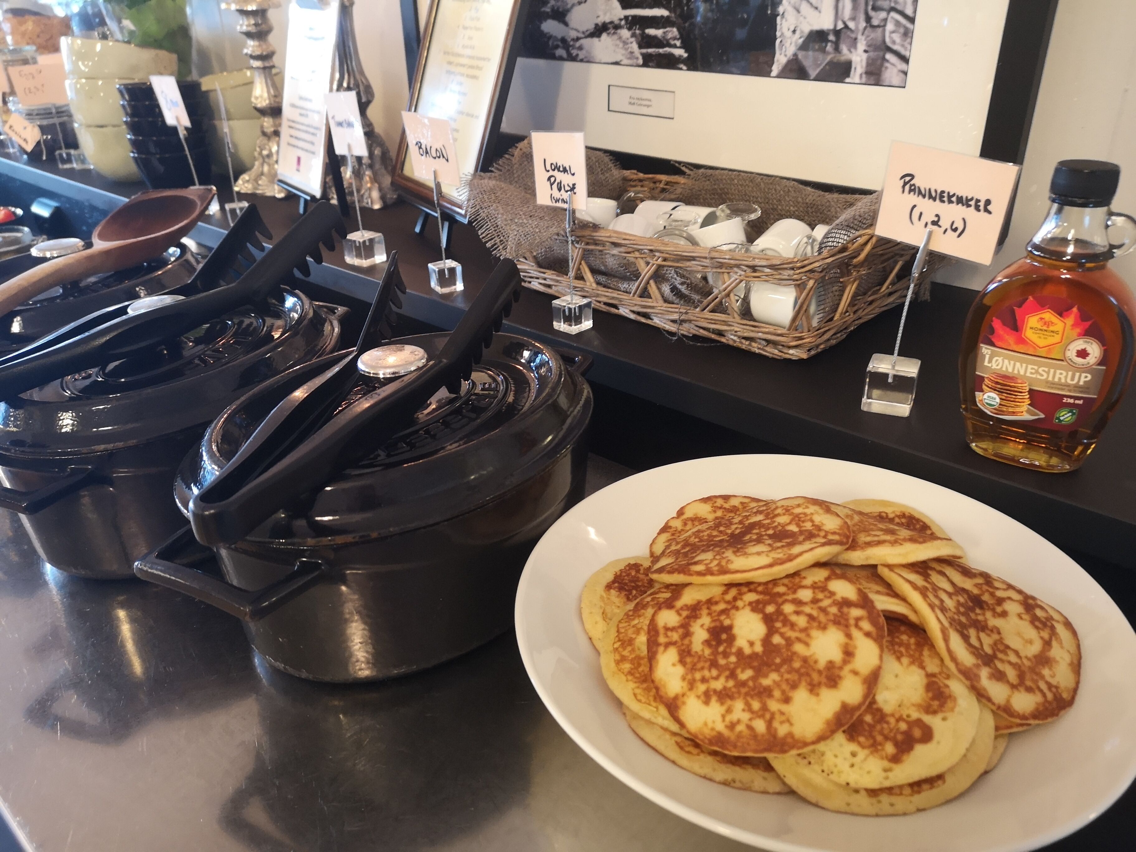 Un desayuno con tortitas, una botella de sirope Lönnesirup y una cesta de huevos.