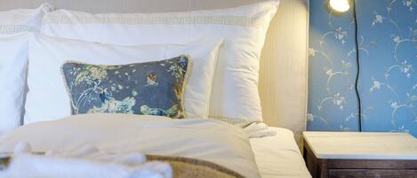 Un lit bien fait, avec du linge de lit blanc et un coussin décoratif, une lampe de chevet et une table de chevet en bois.