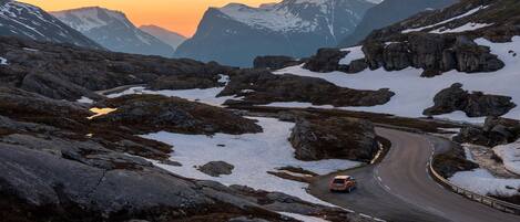 A winding mountain road with snow patches and rocky terrain.