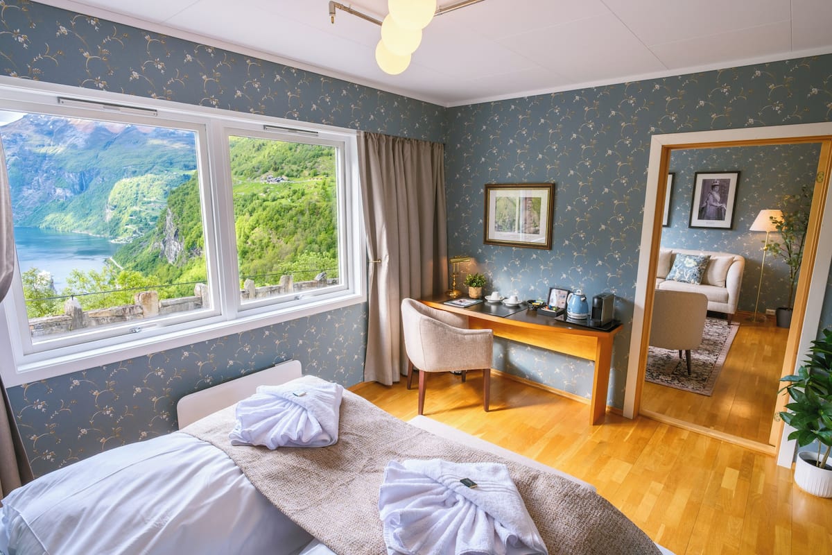 A hotel room with a bed, a desk, and a view of a mountainous landscape.