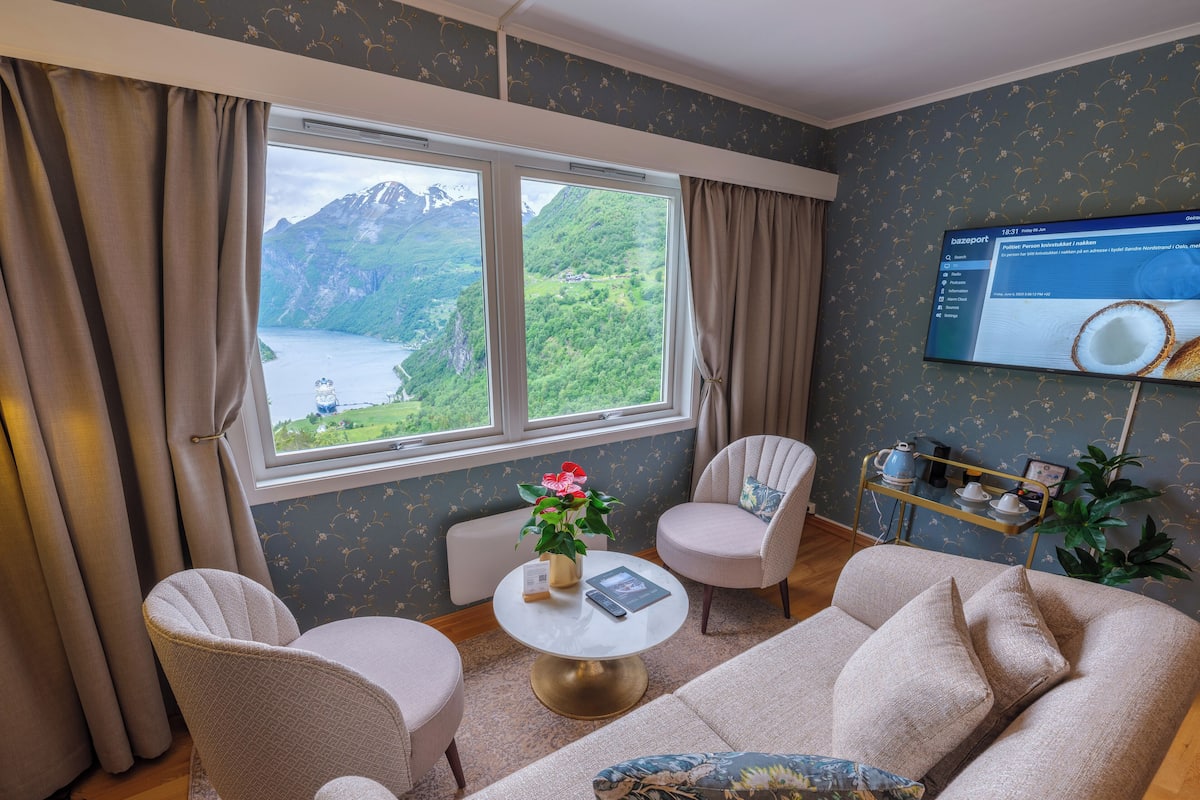 A cozy room with a sofa, two armchairs, a small table with a vase of flowers, and a TV on the wall.