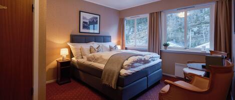 Un dormitorio con cama, mesita de noche, silla y ventana con vistas a árboles.