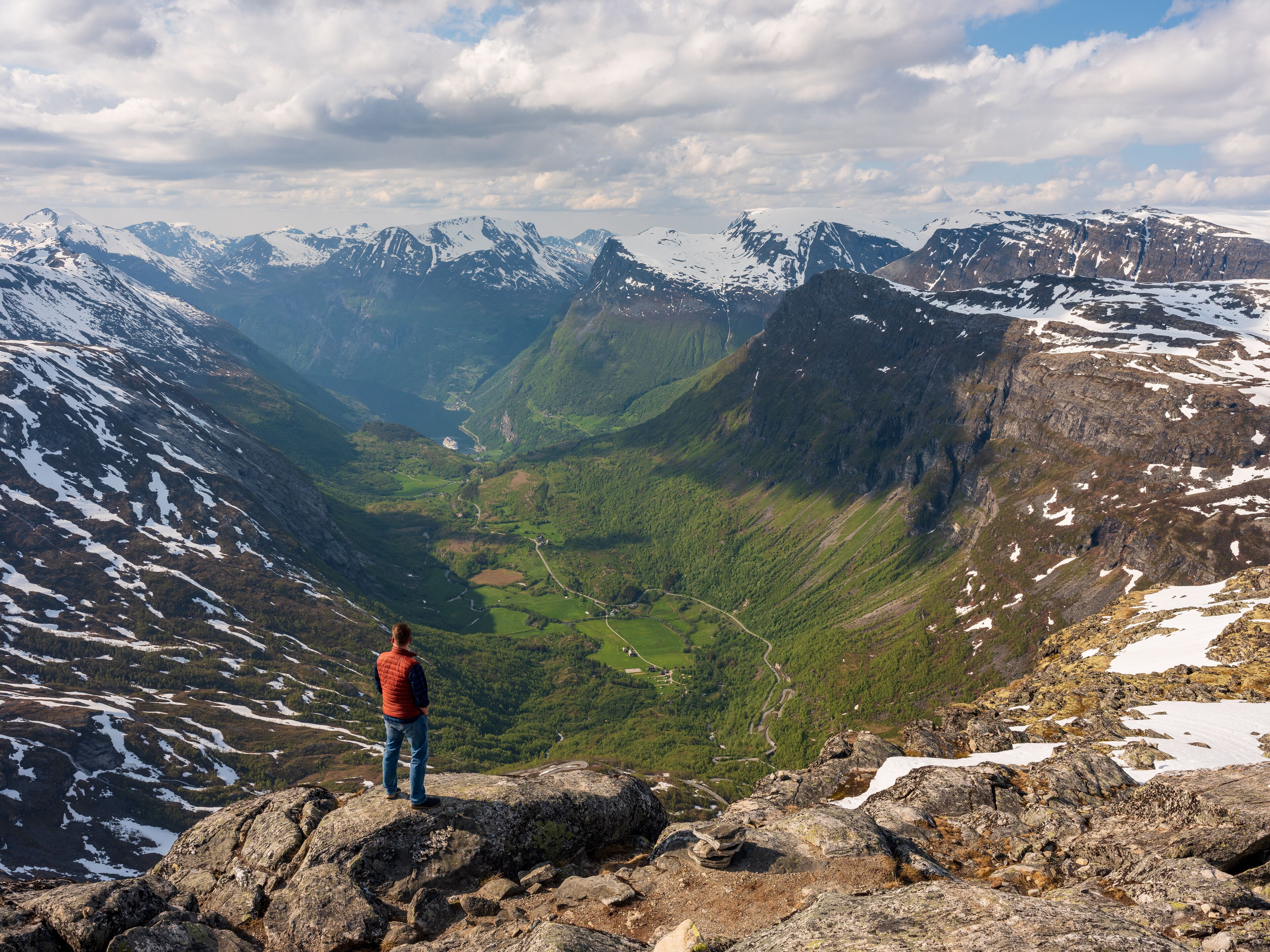 A person standing on a rocky outcrop overlooking a valley with mountains in the distance.