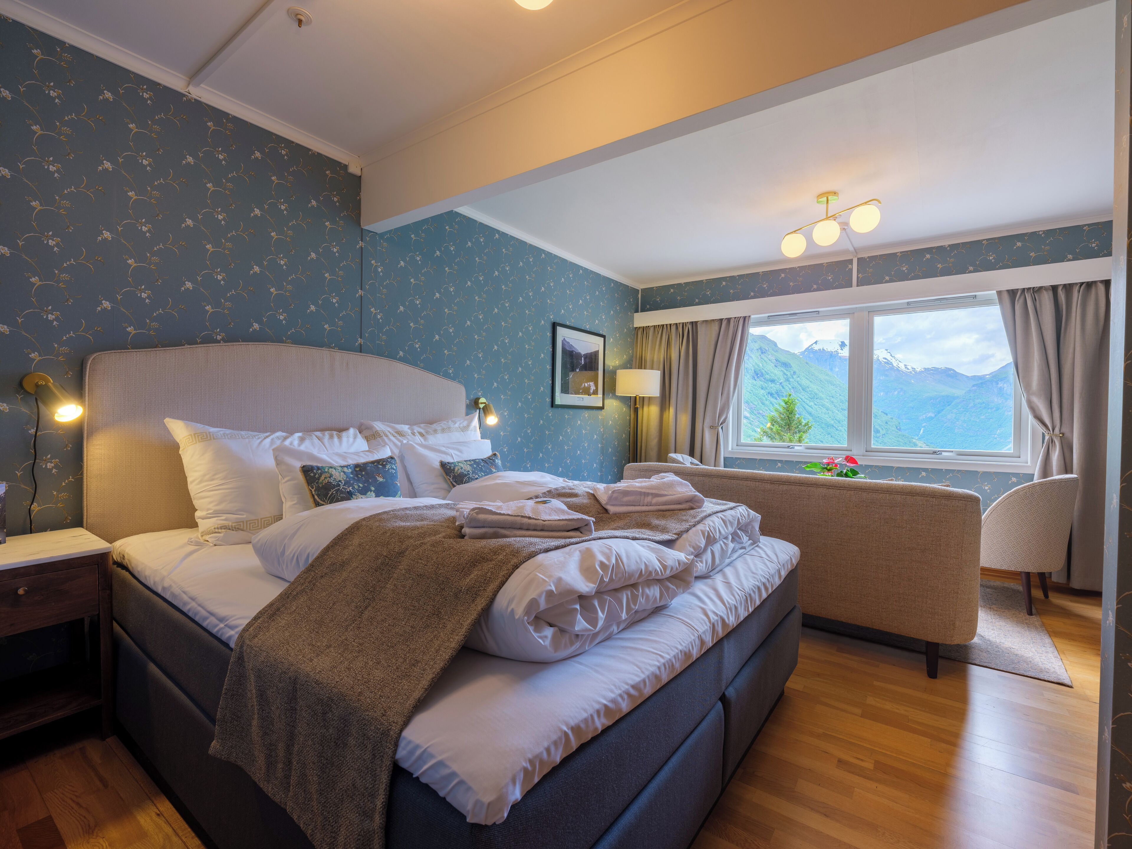 Un dormitorio con cama, mesita de noche, lámpara y ventana con vistas a la montaña.