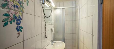 A bathroom with a sink, a hairdryer, and a shower enclosure.