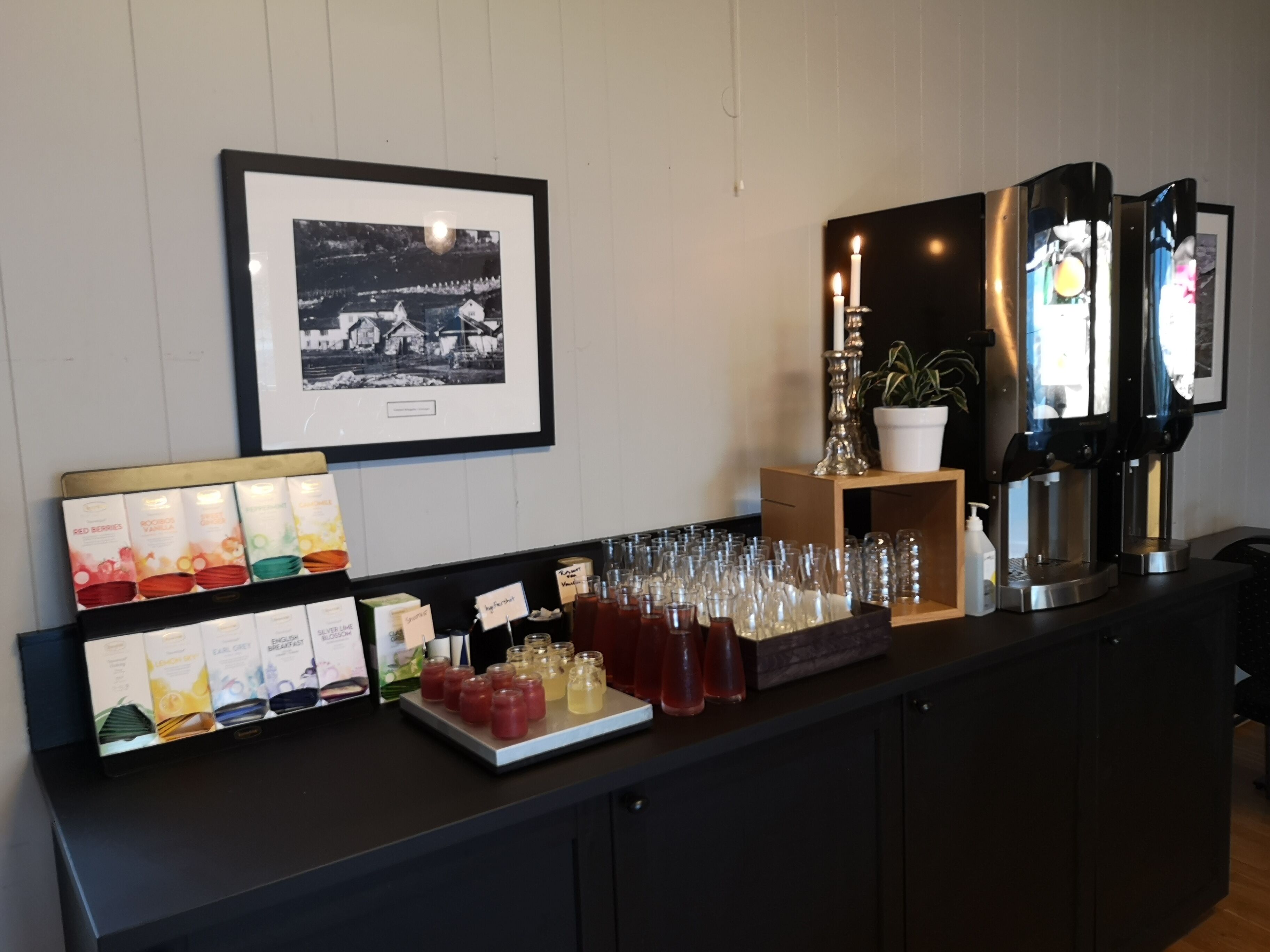 Un mostrador de buffet con diversas opciones de comida y bebidas, un cuadro en la pared y una máquina de café.