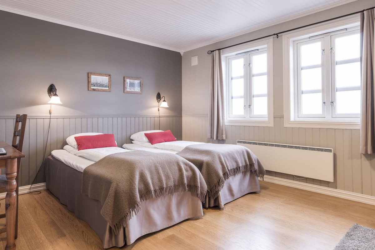 Habitación con dos camas, un escritorio y una silla. Cuenta con dos lámparas de pared, un radiador y una ventana con cortinas.