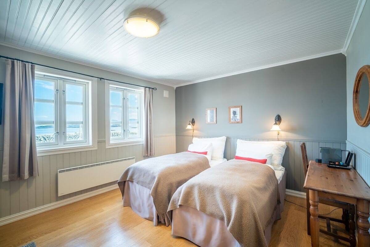 Una habitación con dos camas, una mesa de madera y vistas al mar a través de amplios ventanales.