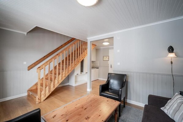 A living room with a wooden staircase, a black leather chair, and a dining table.