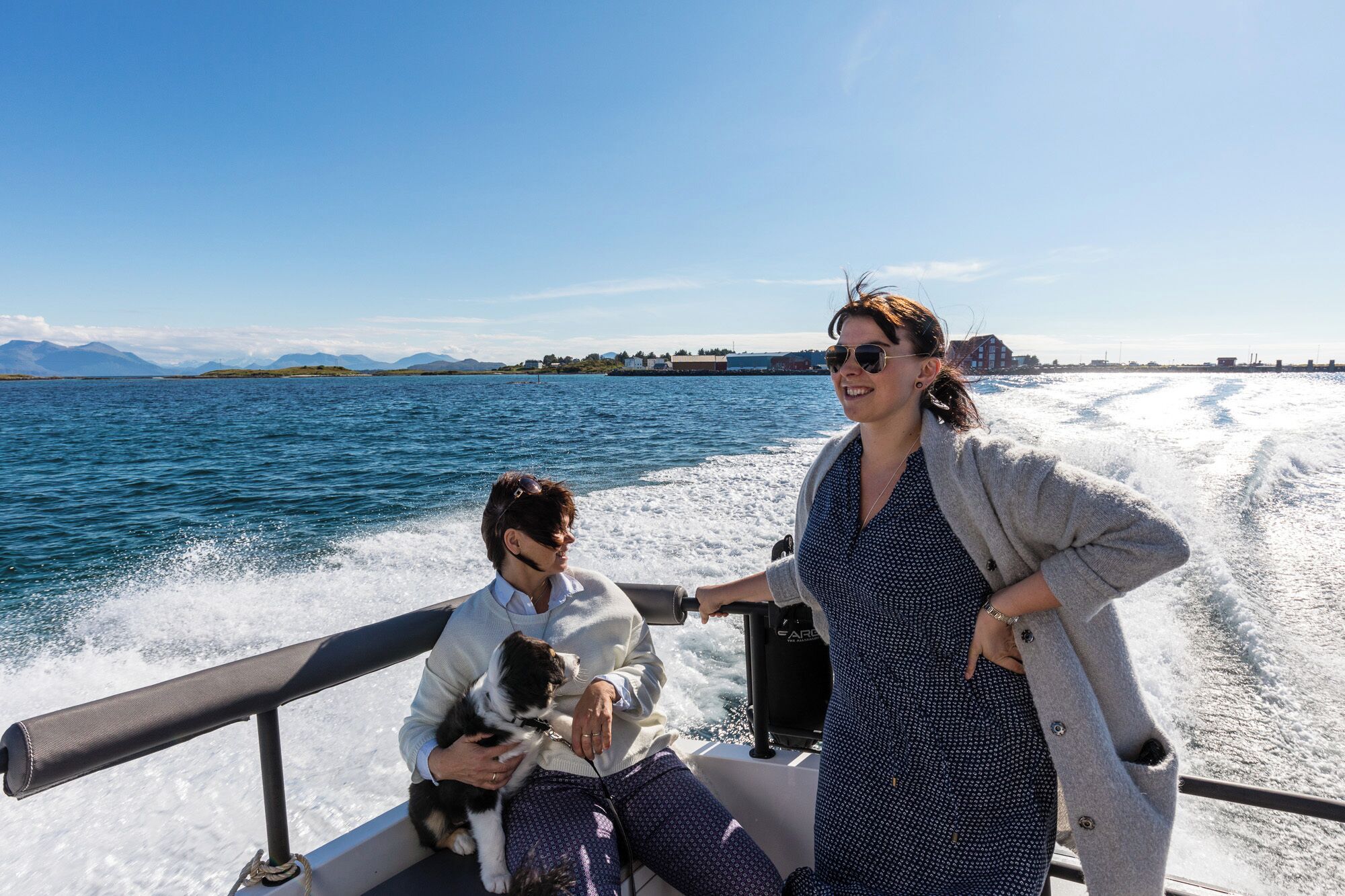 A boat with two people and a dog, with a clear view of the water and distant land.