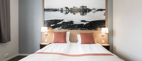 A hotel room with a large bed, two bedside lamps, and a wall-mounted artwork depicting a landscape.