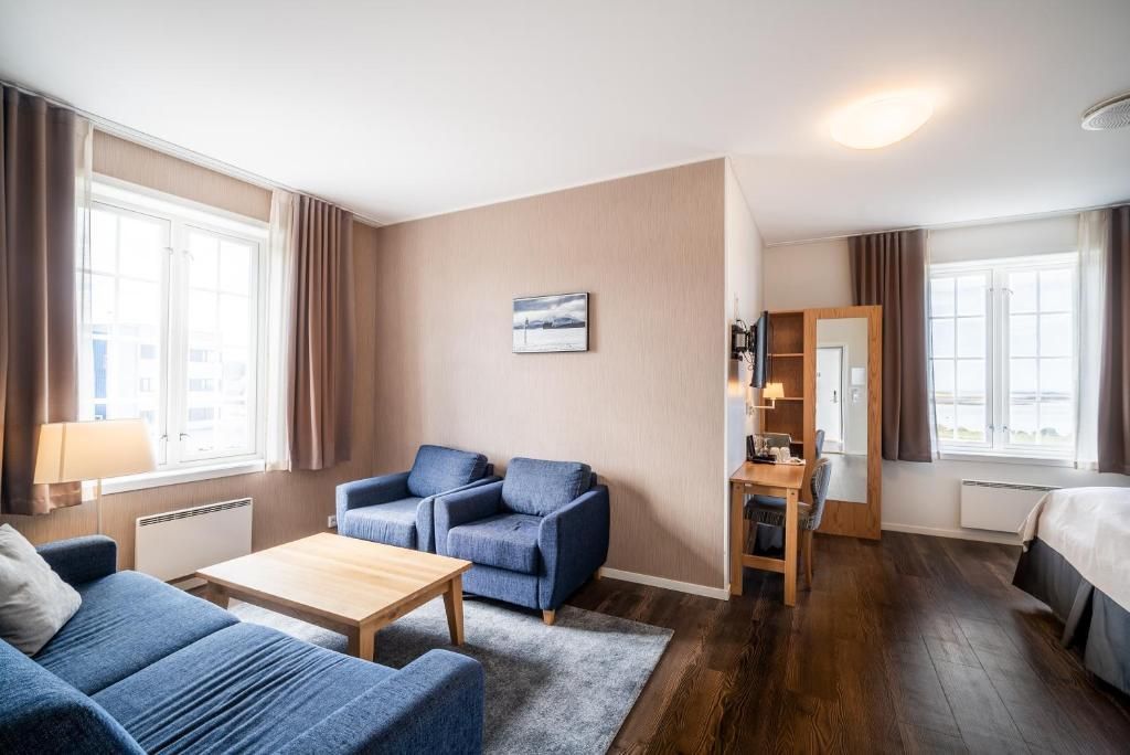 Ein Hotelzimmer mit einer Couch, einem kleinen Tisch, einem Schreibtisch, einem Bett und einem Fenster mit Vorhängen.