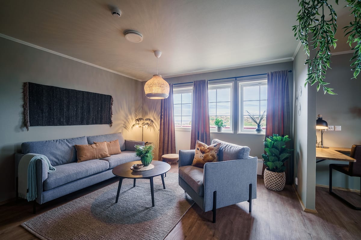 A modern living room with a sofa, armchair, coffee table, and a hanging light fixture.